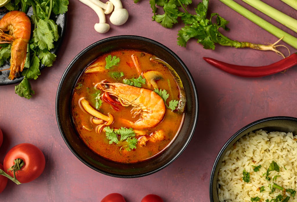 A mouthwatering bowl of Tom Yum soup with shrimp, mushrooms, and herbs, perfect for Asian cuisine enthusiasts.